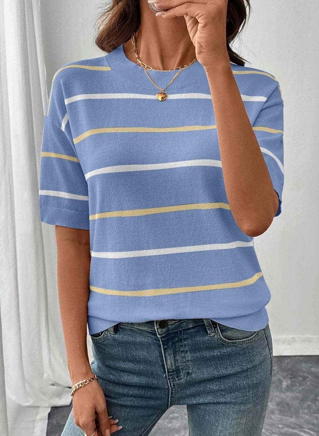 A woman wearing a short-sleeve crewneck knit top with horizontal stripes in light blue, white, and pale yellow, paired with blue jeans.