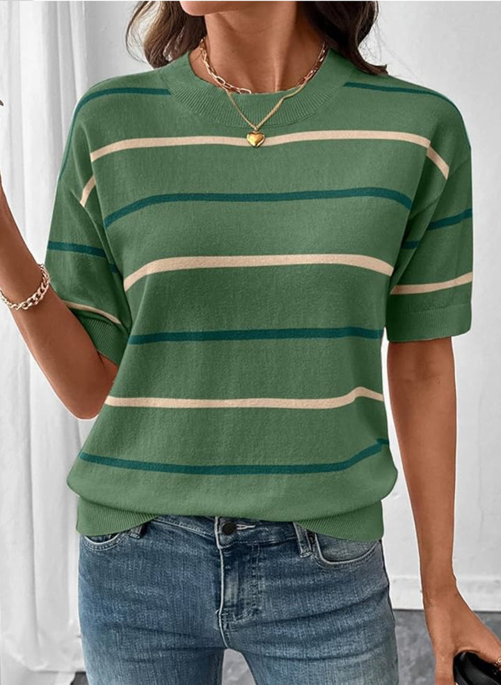 Person wearing a green and beige striped shirt with blue jeans indoors.