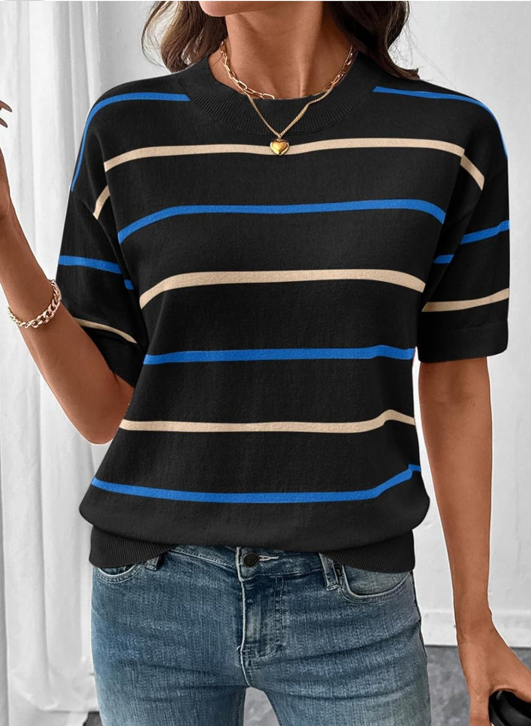 Person wearing a black striped shirt with blue and beige lines, standing against a white curtain.